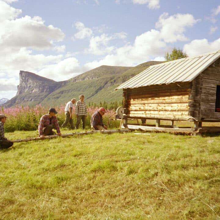 Skierfeklippan i bakgrunden. I förgrunden arbetar människor bredvid ett litet timmerhus